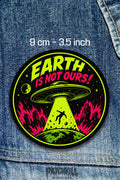 Earth Is Not Ours UFO alien circle patch with neon green and pink flying saucer abduction design on denim jacket